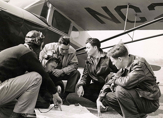 Group of trainees in huddled under a plane for the civilian pilot training program